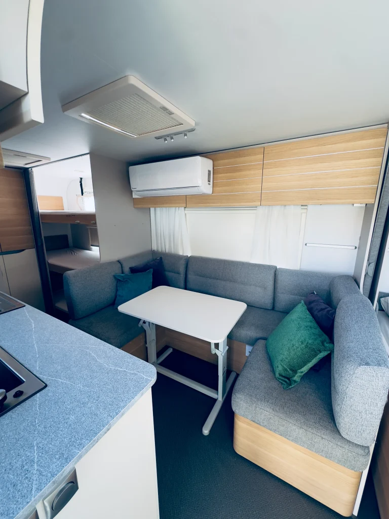 אזור הסלון בקרוואן Adria 573PT כולל מזגן ושולחן מתקפל.